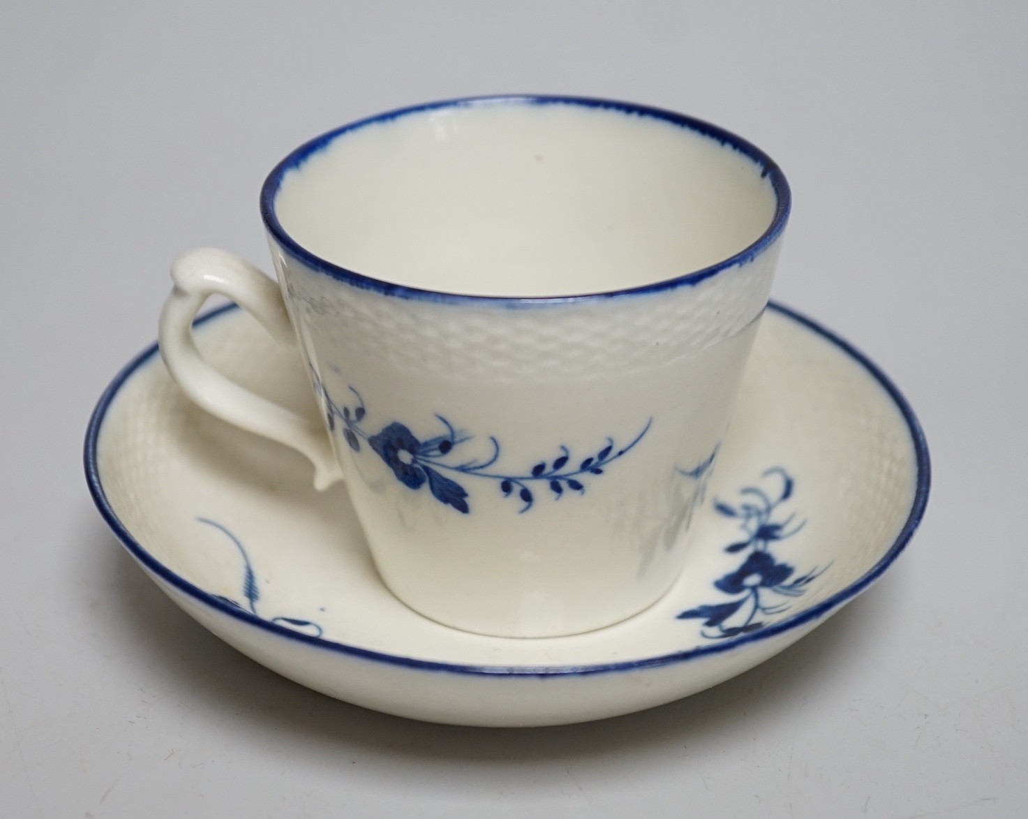 An 18th century Caughley coffee cup and saucer, Chantilly sprigs under a basket weave moulded border, saucer 13cms diameter